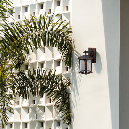 Bronze metal outdoor wall light lifestyle image with fluted glass shade mounted on white villa wall with palm trees.
