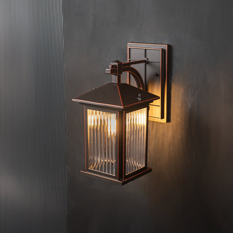 Decorative lantern wall sconce with ribbed glass glowing warmly on a black background.