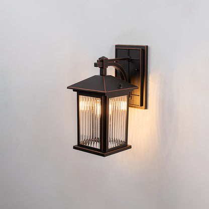 Bronze metal outdoor wall light on white background with ribbed glass shade illuminating a warm light for patio decor.
