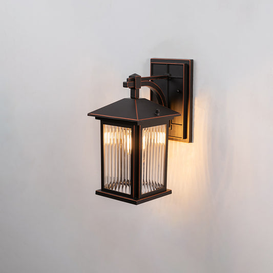 Bronze metal outdoor wall light on white background with ribbed glass shade illuminating a warm light for patio decor.