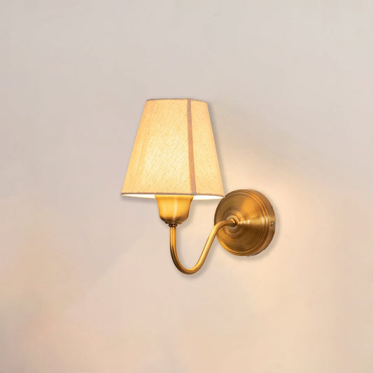 Traditional brass wall light fixture with white shade switched on radiating soft warm glow on minimal white backdrop.