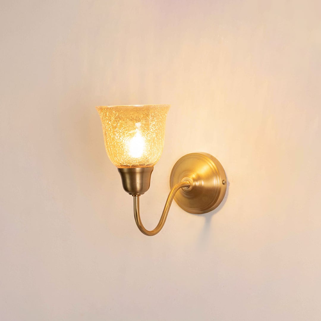 Vintage gold gooseneck wall light fixture with a textured amber glass cup shade turned on against a plain background.