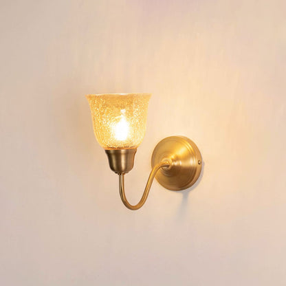 Vintage gold gooseneck wall light fixture with a textured amber glass cup shade turned on against a plain background.