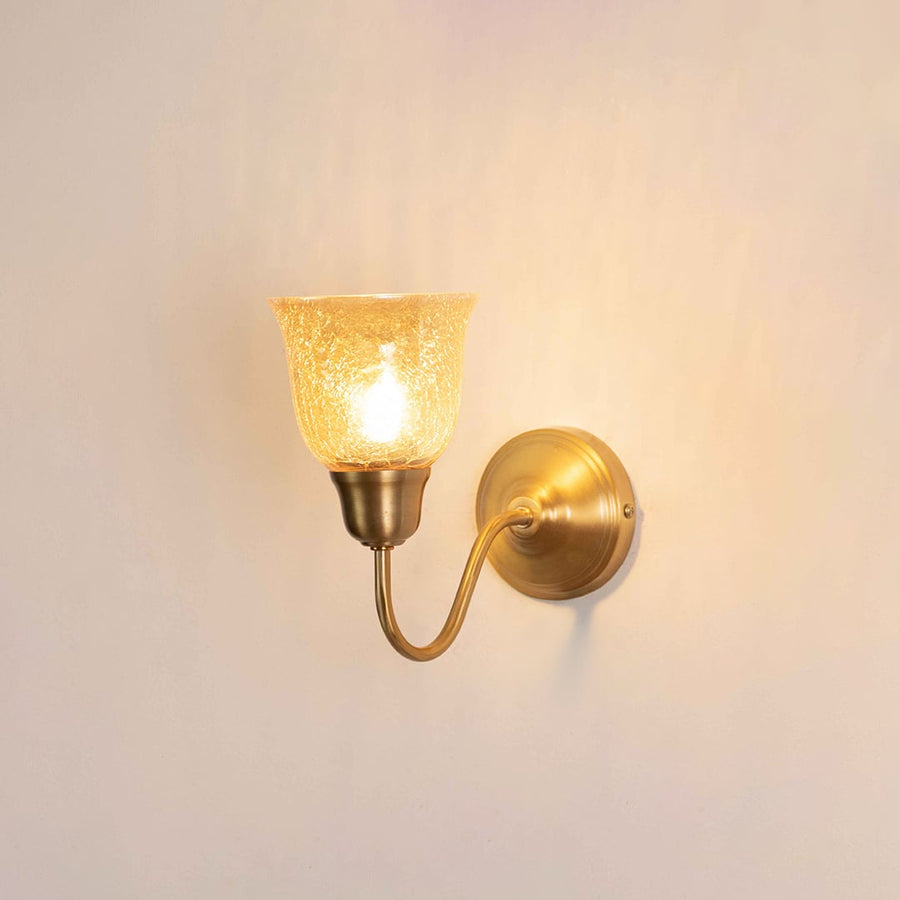 Vintage gold gooseneck wall light fixture with a textured amber glass cup shade turned on against a plain background.