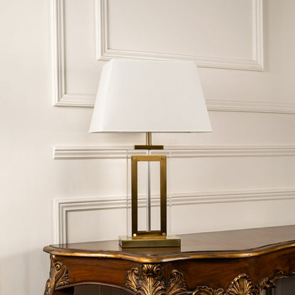 Modern gold table lamp with rectangular design and crisp white shade placed on a plain white background with light turned off.