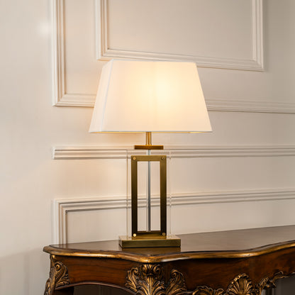 Gold metal table lamp with geometric frame and fabric drum shade offering refined contemporary ambient lighting indoors.