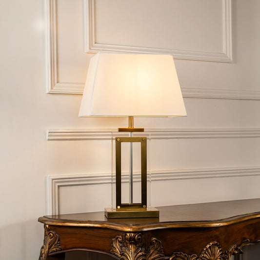 Gold metal table lamp with geometric frame and fabric drum shade offering refined contemporary ambient lighting indoors.
