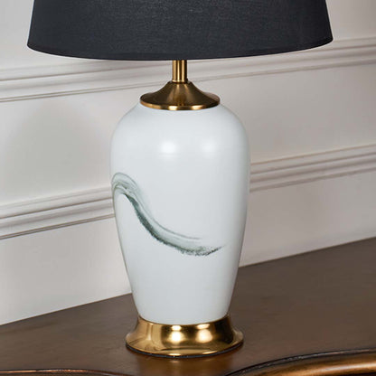 Closeup of white ceramic lamp with soft green brushstroke design gold base and black tapered shade showcasing refined craftsmanship and modern artistic style.