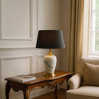 White ceramic table lamp with soft green brushstroke design gold base and black shade placed on a carved wooden side table adding a warm elegant touch to living room decor.