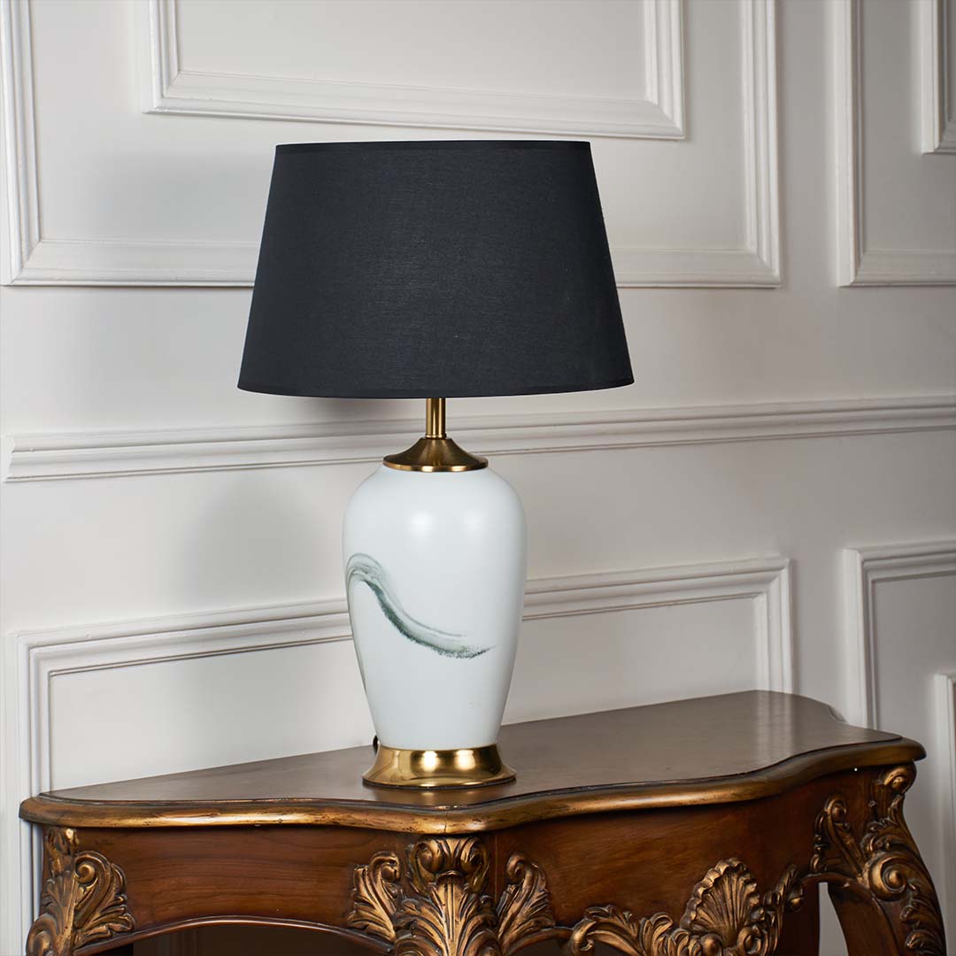 White ceramic lamp with soft green artistic design gold base and black shade shown unlit on a plain white background highlighting its modern elegant form.
