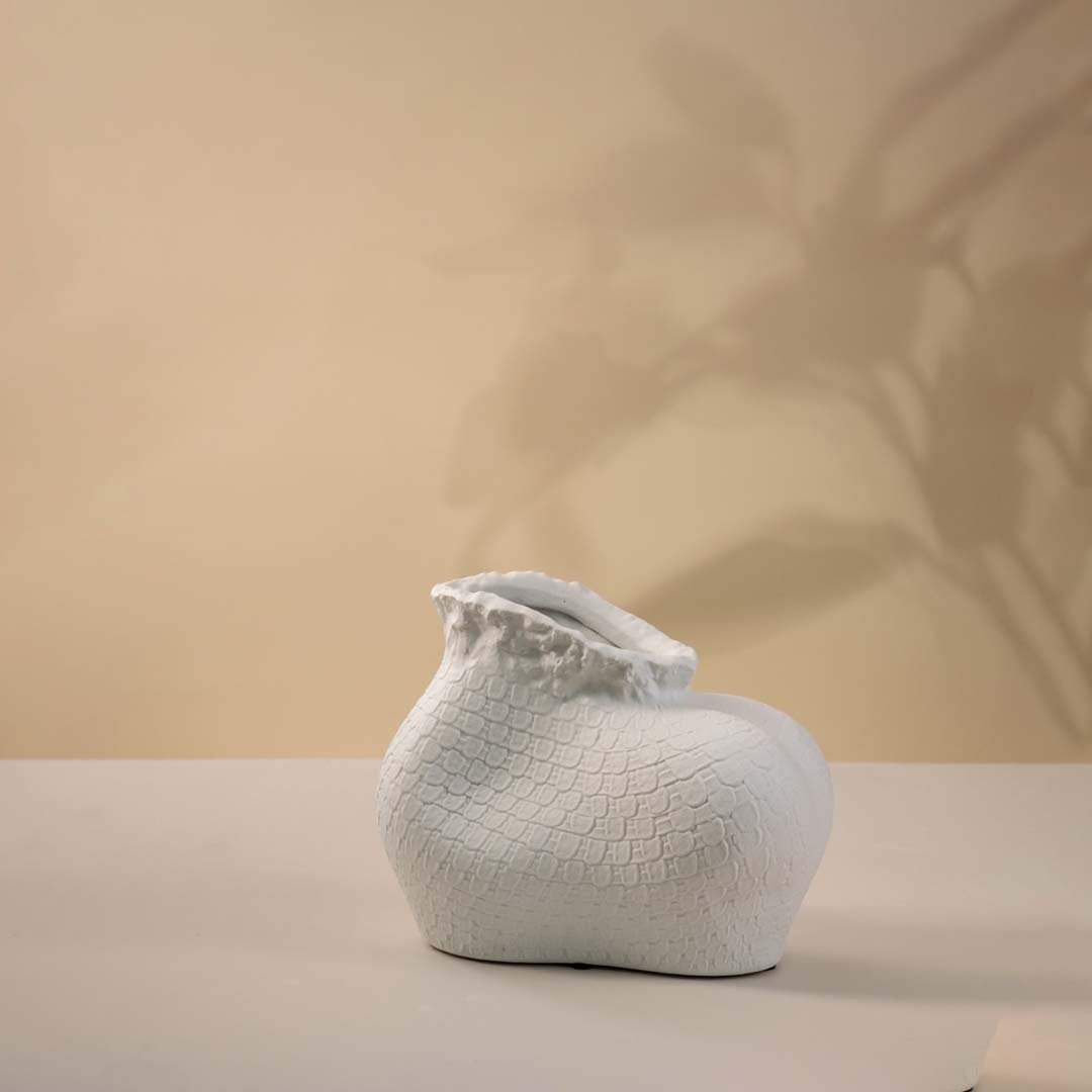 Single white textured ceramic vase with sculptural organic shape and matte finish placed on a plain white surface.