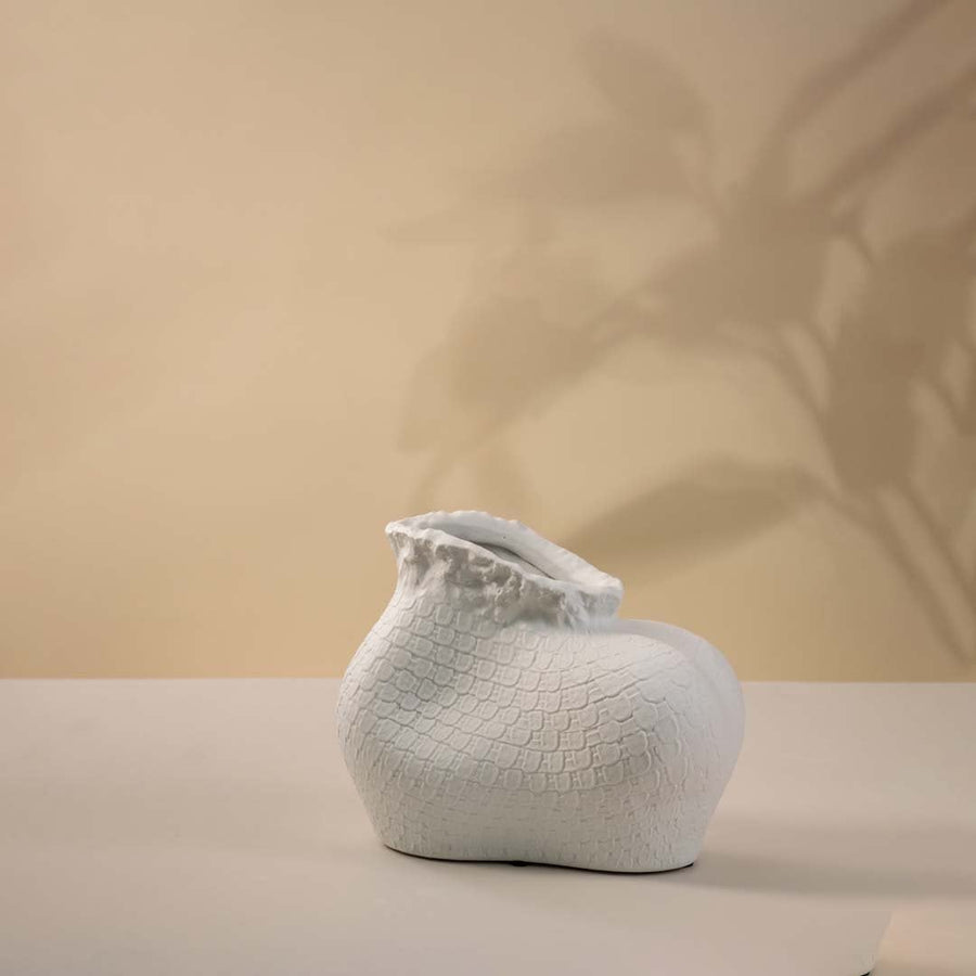 Single white textured ceramic vase with sculptural organic shape and matte finish placed on a plain white surface.