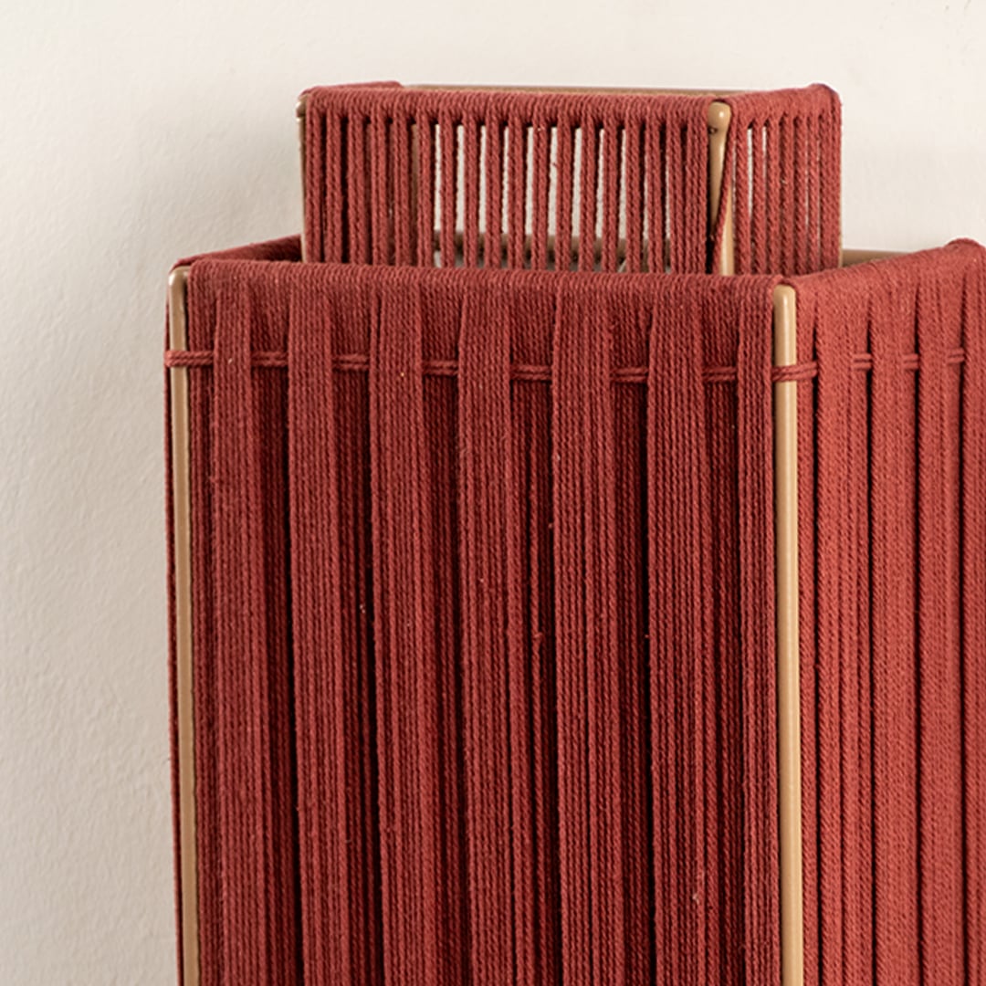 Closeup of red jute wall lamp reveals fine woven details and expert craftsmanship that exude warmth and natural sophistication.