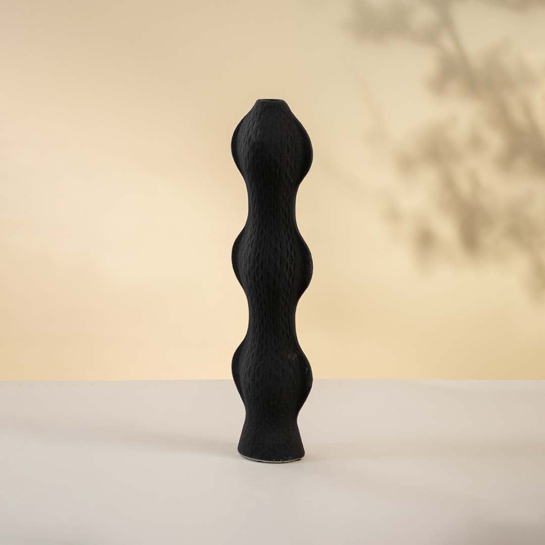 Contemporary black vase softly lit against a white backdrop highlighting its artistic shape and surface texture.