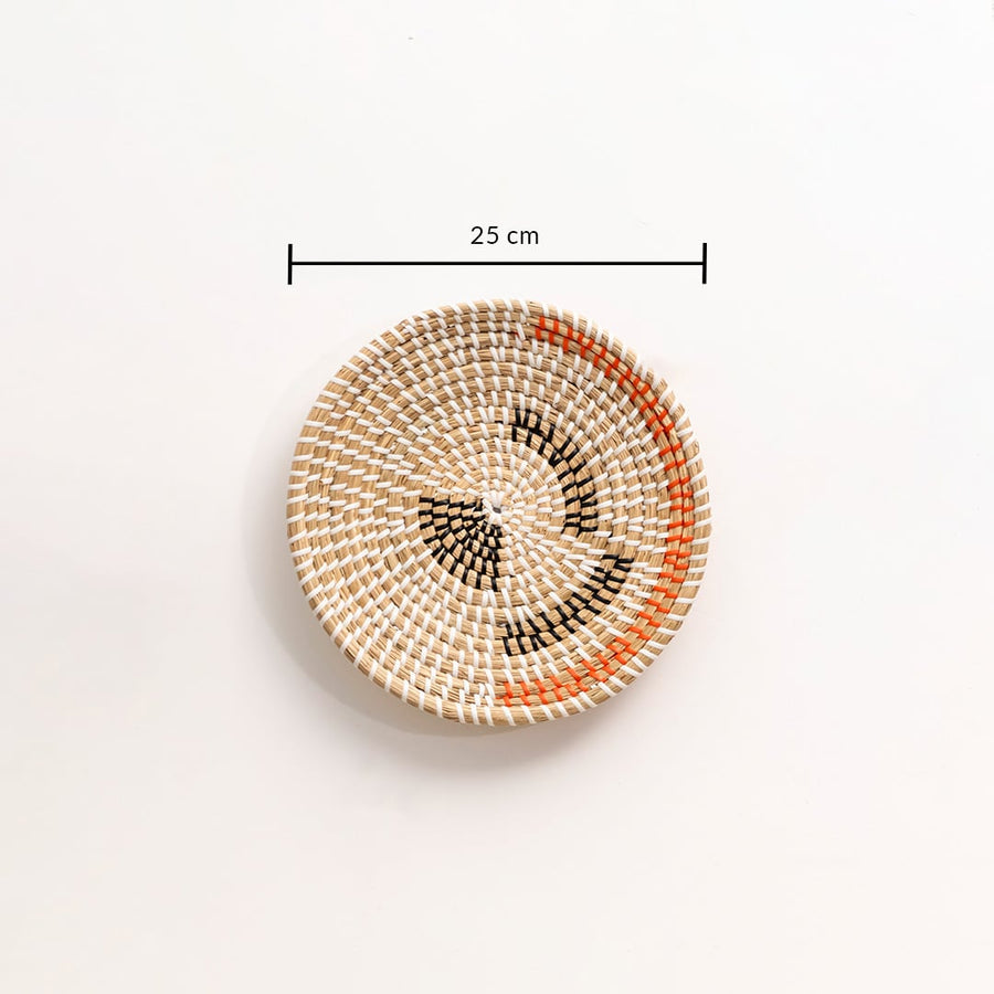 Handwoven wicker basket wall decor in beige with black and orange woven design showing 25 cm size measurement on white.