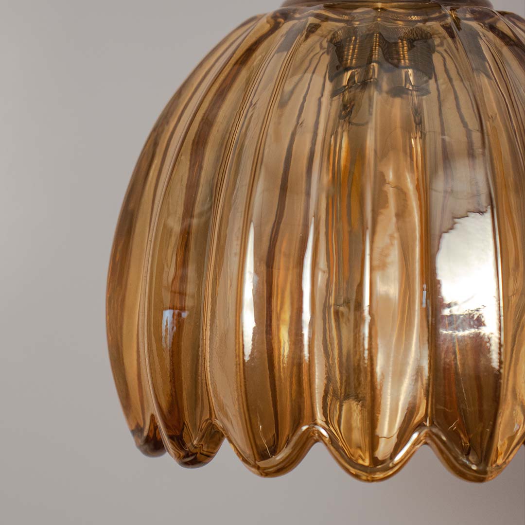 Closeup amber ribbed glass pendant light with warm tone and gold fitting placed against neutral wall background highlighting decorative lighting design.