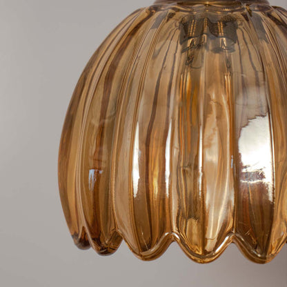Closeup amber ribbed glass pendant light with warm tone and gold fitting placed against neutral wall background highlighting decorative lighting design.
