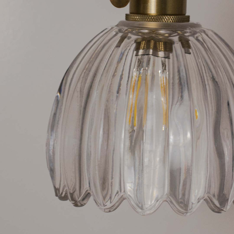Clear ribbed glass pendant light with gold fixture placed against neutral wall background closeup highlighting elegant vintage inspired lighting decor styling.