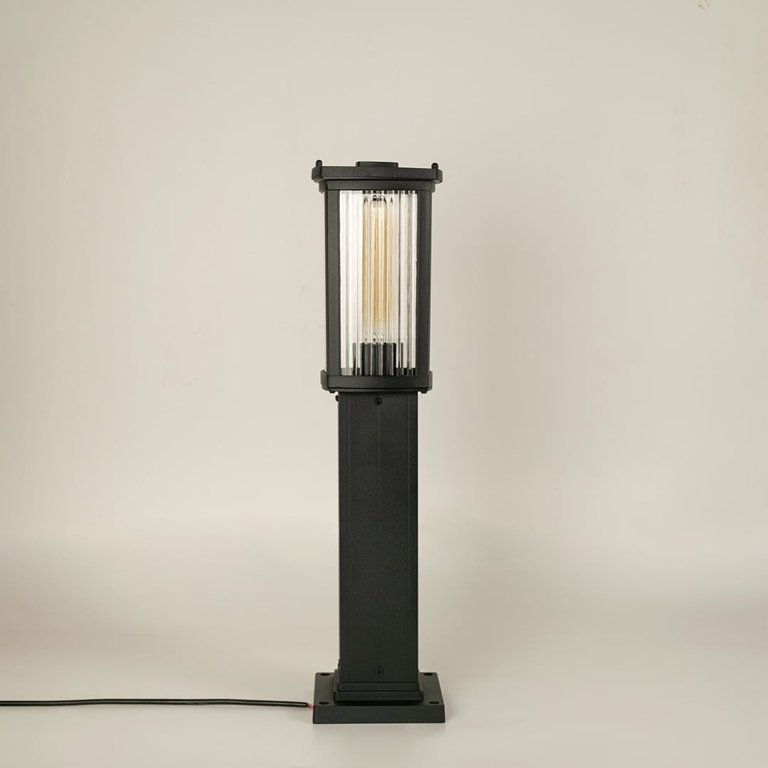 A modern black outdoor bollard light shown on a white background with the light off highlighting its clean rectangular structure clear ribbed glass panels and sturdy base.