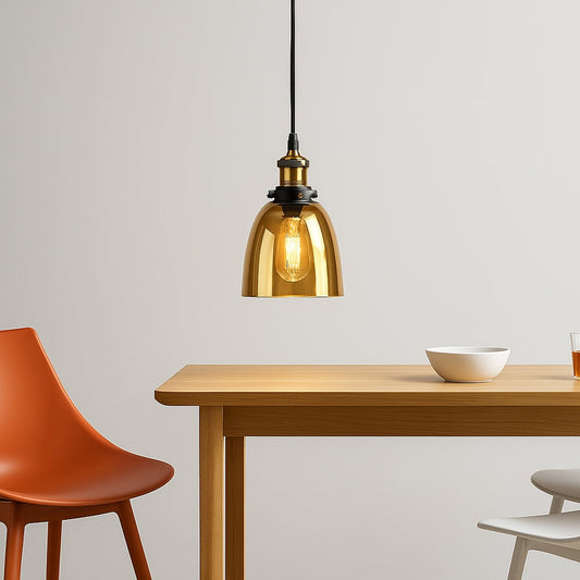 Gold glass pendant light with brass and black holder glowing warmly above modern dining table with chairs.