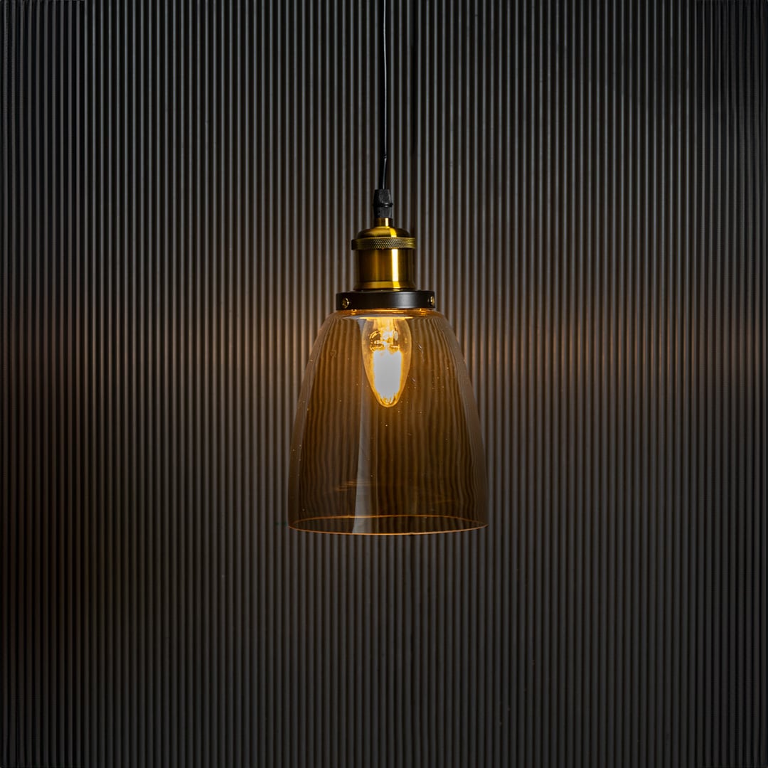 Gold glass pendant light with brass and black holder turned on glowing warmly against plain black background.