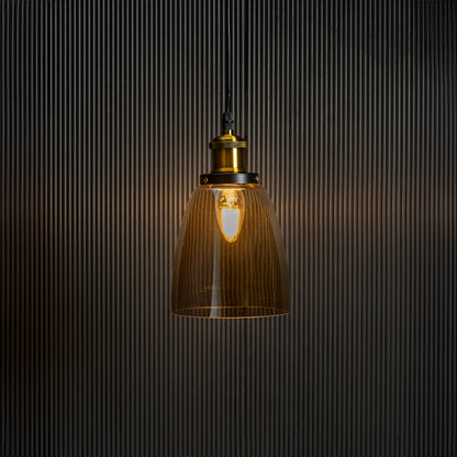 Gold glass pendant light with brass and black holder turned on glowing warmly against plain black background.