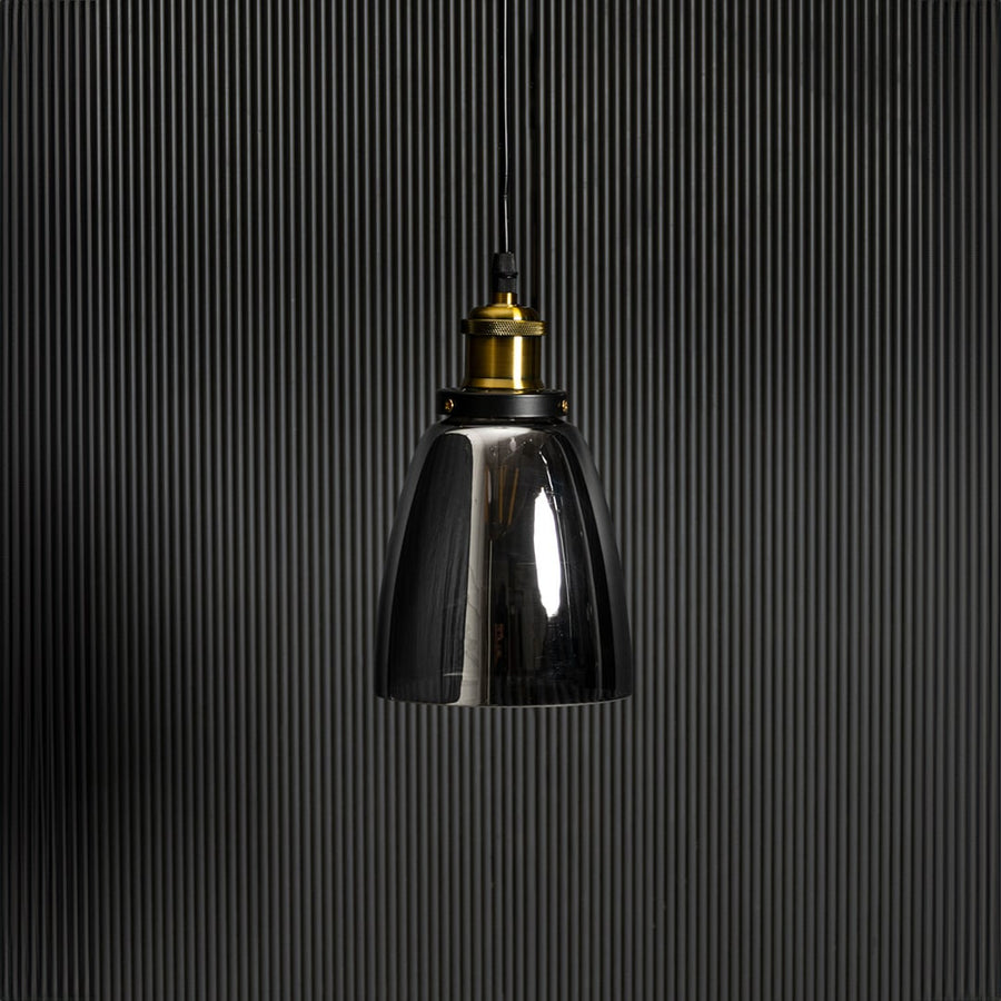 Smoked glass pendant light with brass and black holder in stylish design turned off against black background.
