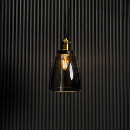 Smoked glass pendant light with brass and black holder turned on glowing softly against plain black background.