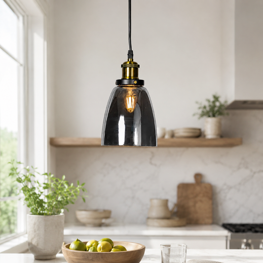 A modern pendant light with a dark smoked glass bell-shaped shade and a brass-finished socket, hanging in a bright, contemporary kitchen.