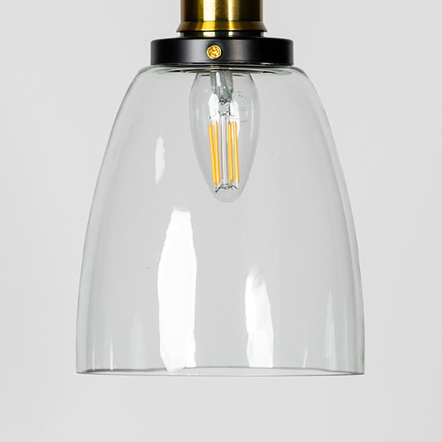 Closeup of clear glass pendant light with brass and black holder showcasing modern minimalist design.