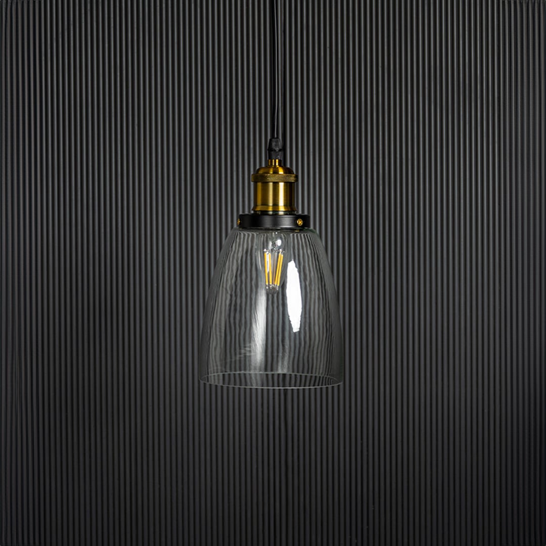 Clear glass pendant light with brass and black holder in modern design turned off on plain white background.
