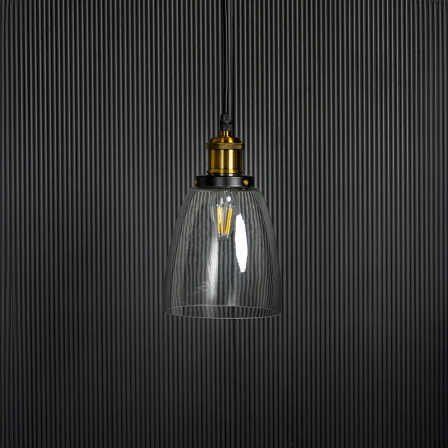Clear glass pendant light with brass and black holder in modern design turned off on plain white background.