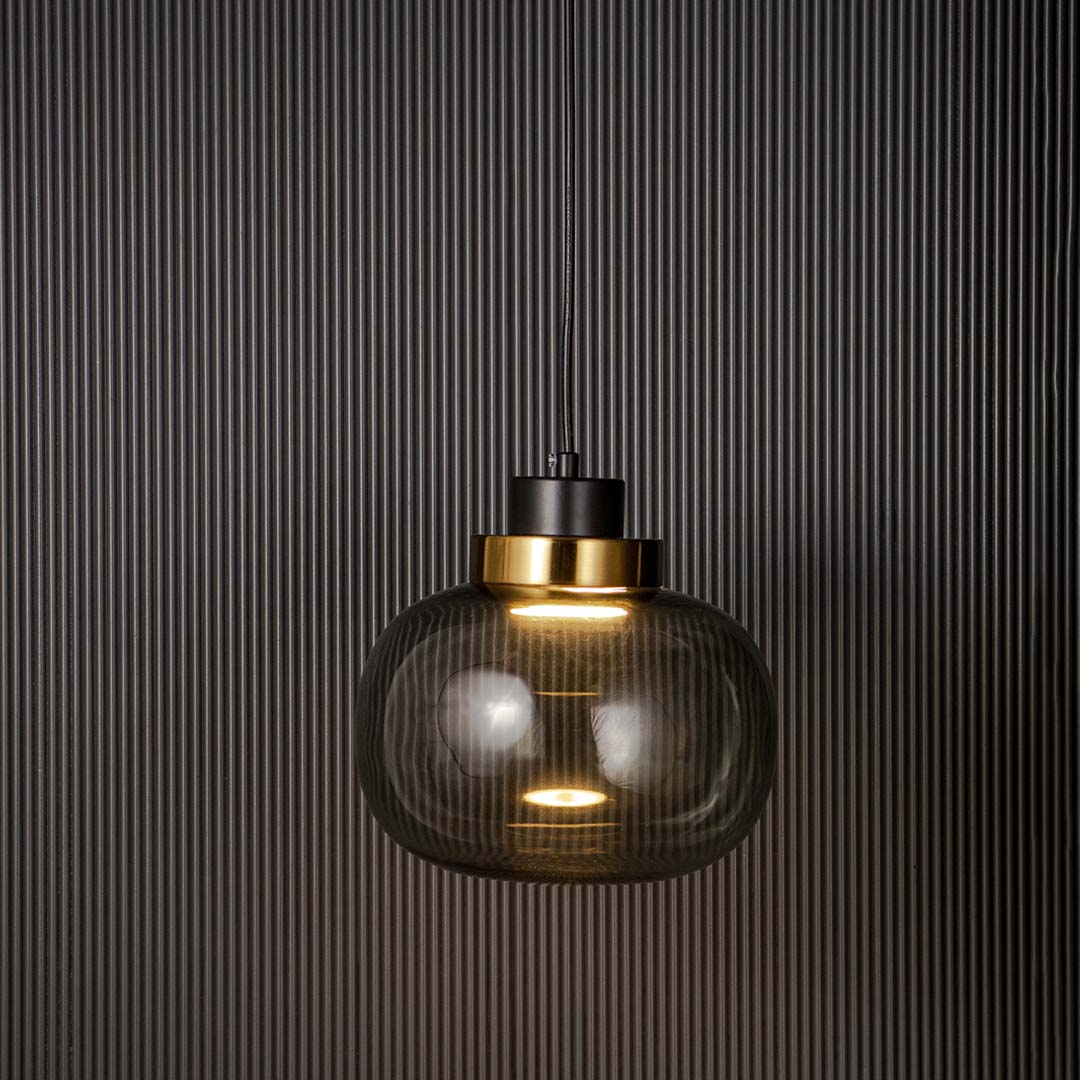 Contemporary smoked glass pendant lamp glowing with warm light golden accent and black cord perfect for dining and living room.