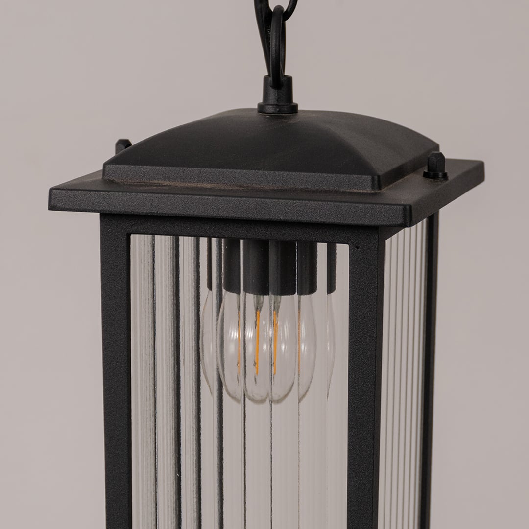 Closeup of black metal hanging lantern showcasing ribbed glass texture and warm bulb detail for outdoor home decor lighting.