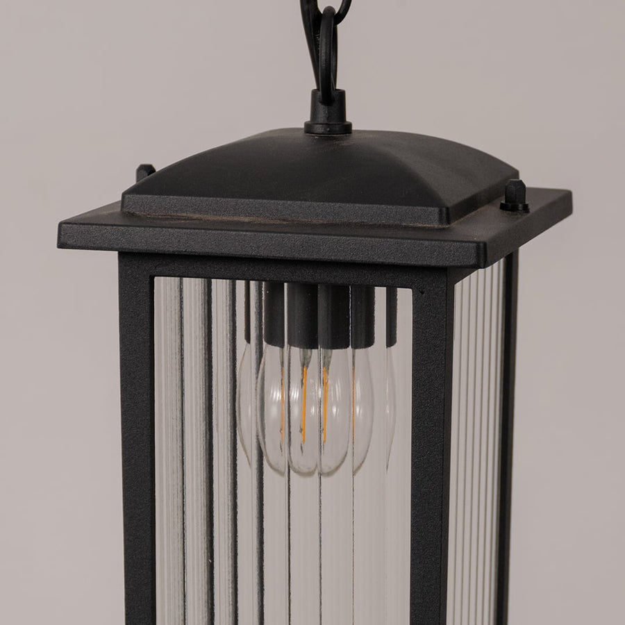 Closeup of black metal hanging lantern showcasing ribbed glass texture and warm bulb detail for outdoor home decor lighting.