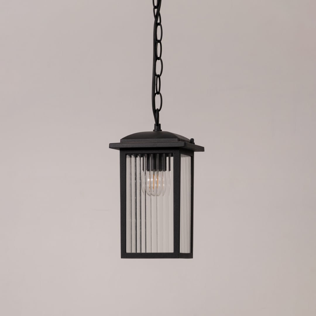 Black metal hanging lantern with ribbed glass shown switched off on white background for outdoor porch and patio decor.