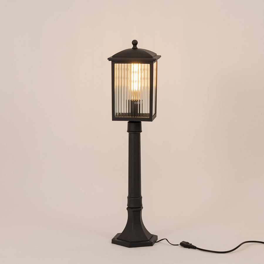 Black outdoor garden light with warm glowing ribbed panels for elegant exterior decor styling use.