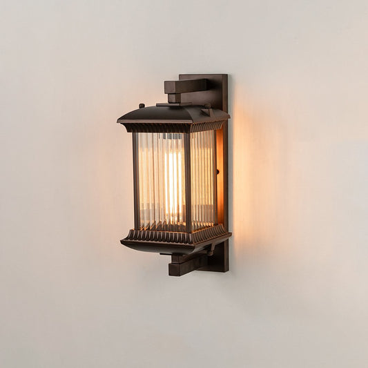Antique bronze metal outdoor wall light on white background with ribbed glass shade illuminating warm patio decor.