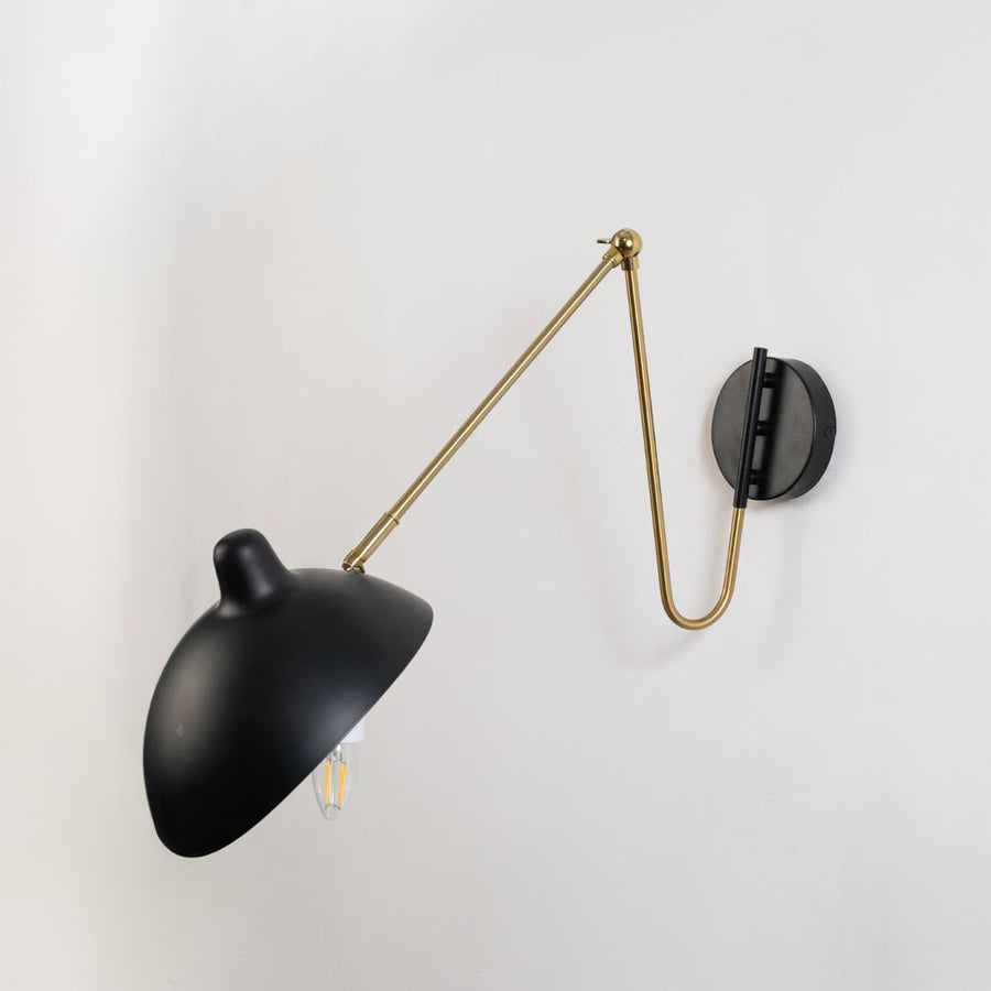 Wall sconce with matte black shade adjustable gold arm and black base designed for modern interiors in bedroom living room and office walls.