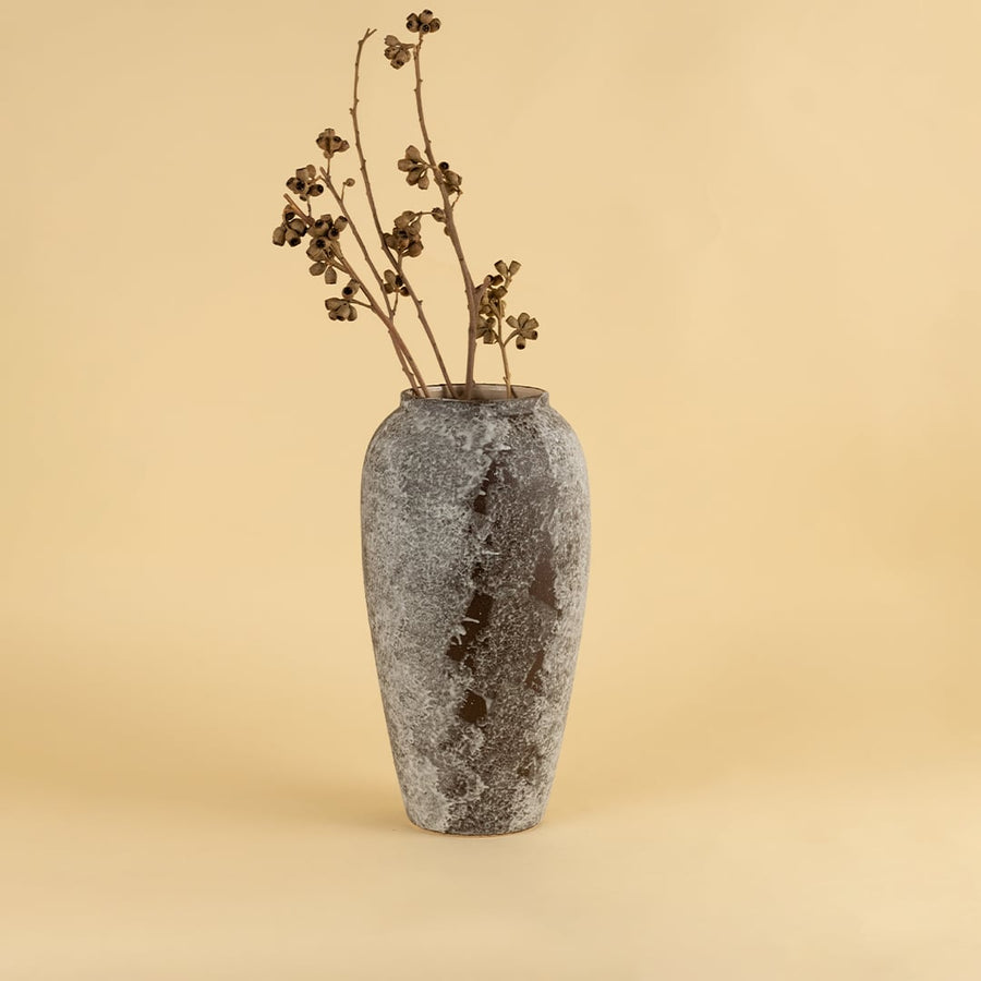 Tall rustic ceramic vase in grey brown textured finish styled with dry stems for modern home interior decoration.
