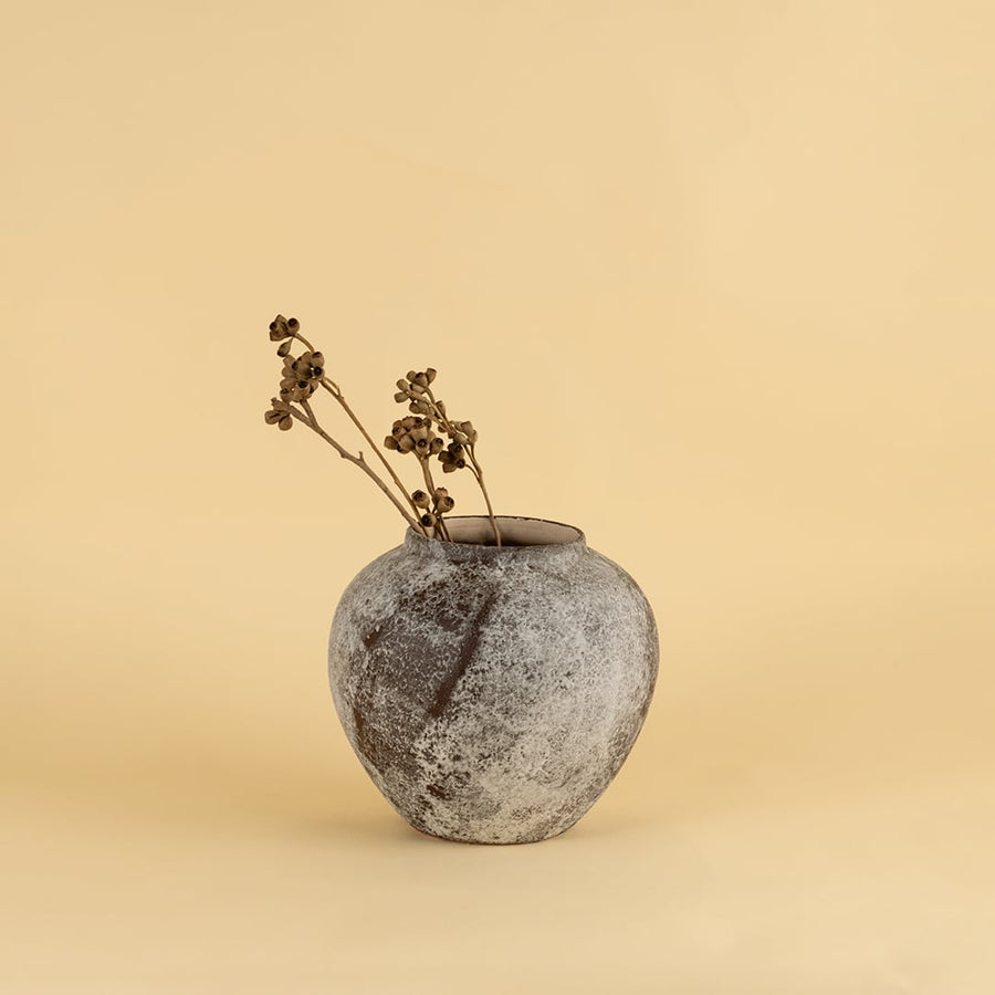 Rustic ceramic vase in grey and brown textured finish with round shape styled with dry stems for home decor.
