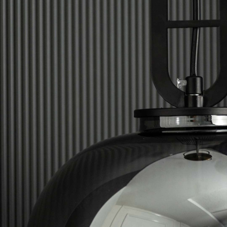A closeup of the smoked glass pendant light highlighting its warm illuminated filament bulb and reflective smooth curved glass design.