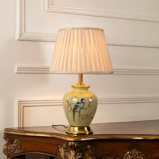 Floral ceramic table lamp with pleated shade casting warm light on wooden side table in a refined interior setting.