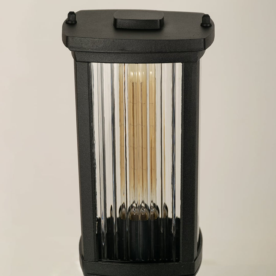 A closeup view of the outdoor bollard light highlighting the ribbed clear glass panels and metallic black frame with detailed texture and clean modern lines.