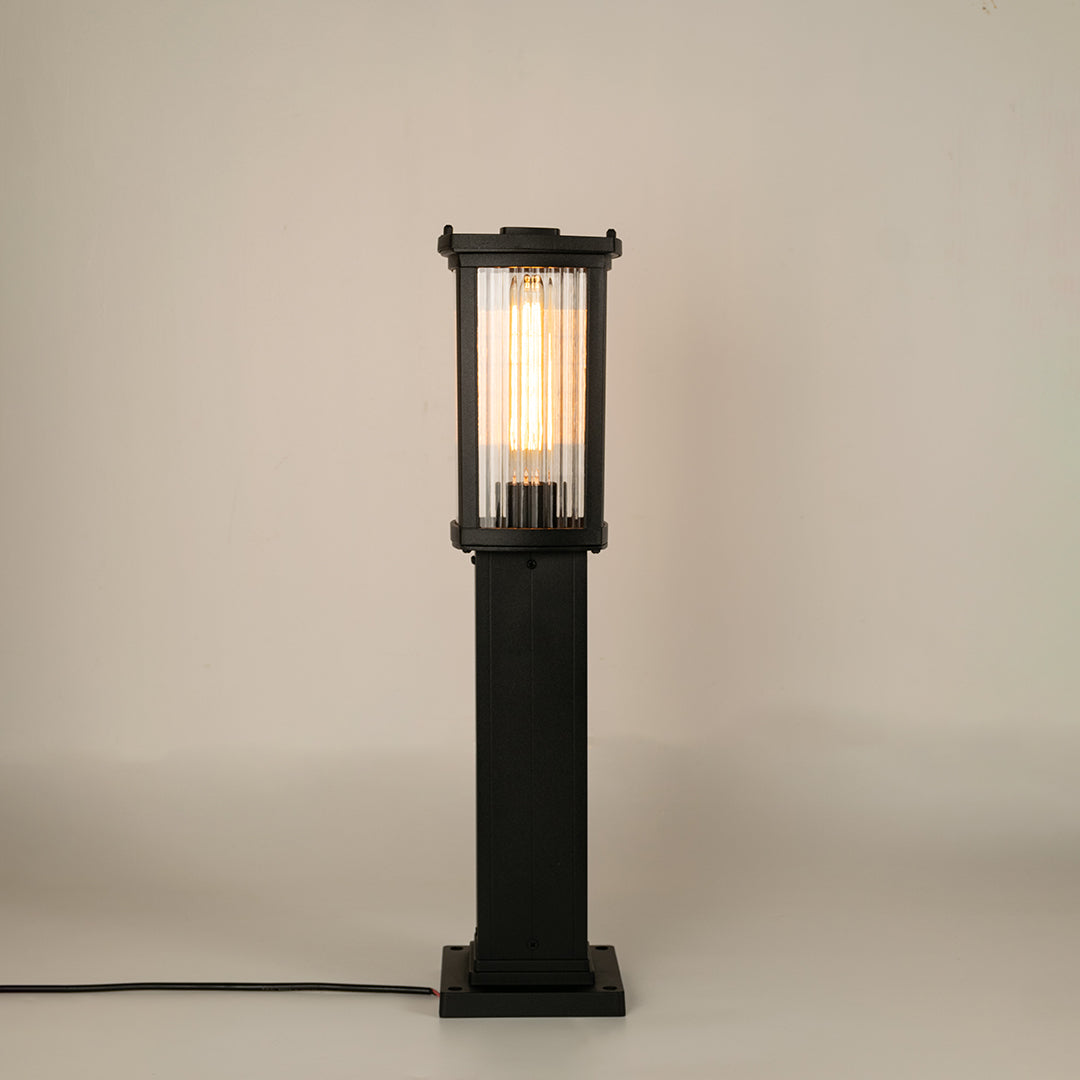 Black outdoor bollard light with ribbed glass panels for stylish garden pathway decor use.