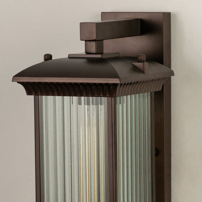 A closeup view of the bronze outdoor wall lantern showing the ribbed glass panels and warm glow highlighting the refined craftsmanship and elegant finish.