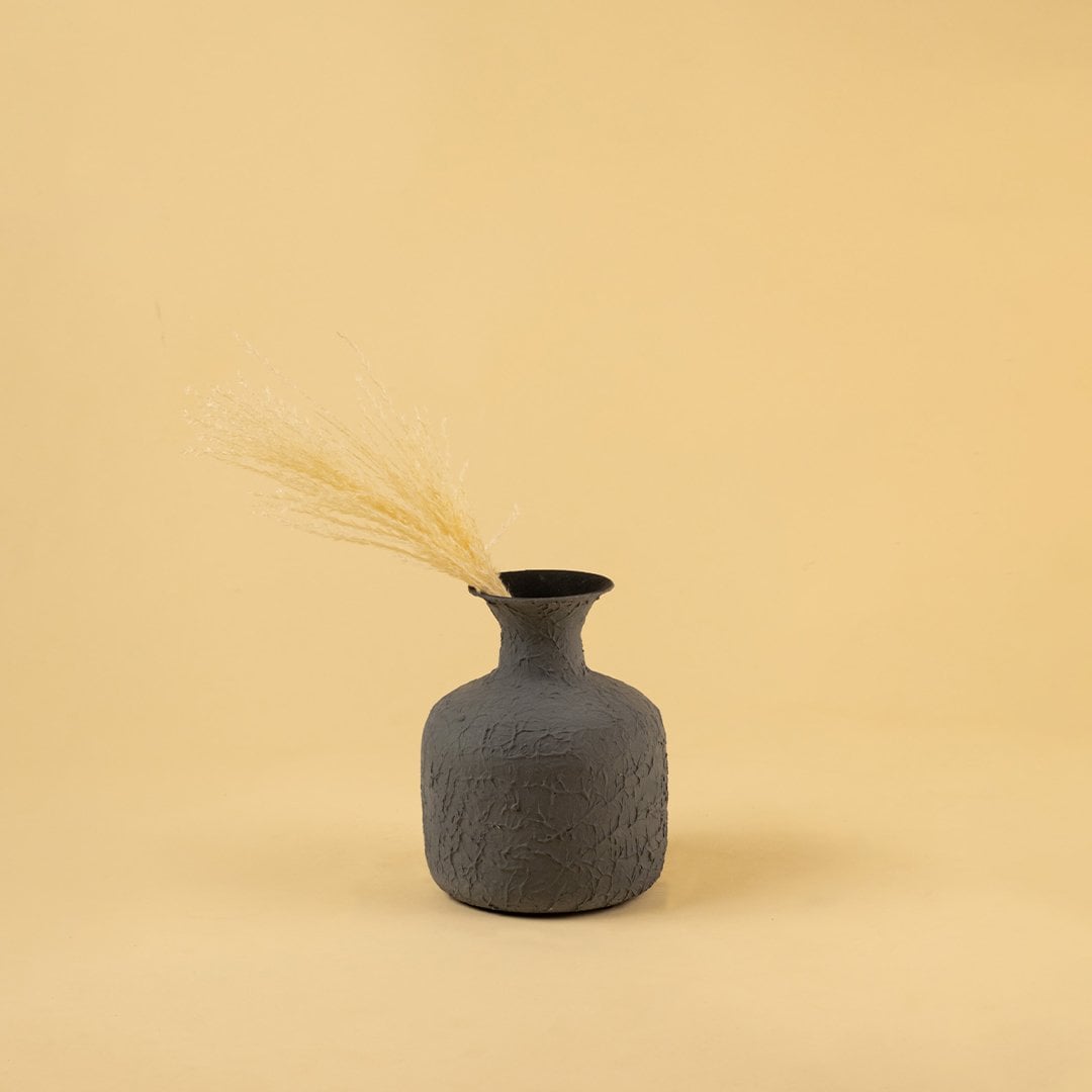 A grey vase with dry grass displayed in a minimal earthy setup highlighting its rustic texture and simple styling against a warm beige backdrop.