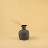 A grey vase with dry grass displayed in a minimal earthy setup highlighting its rustic texture and simple styling against a warm beige backdrop.