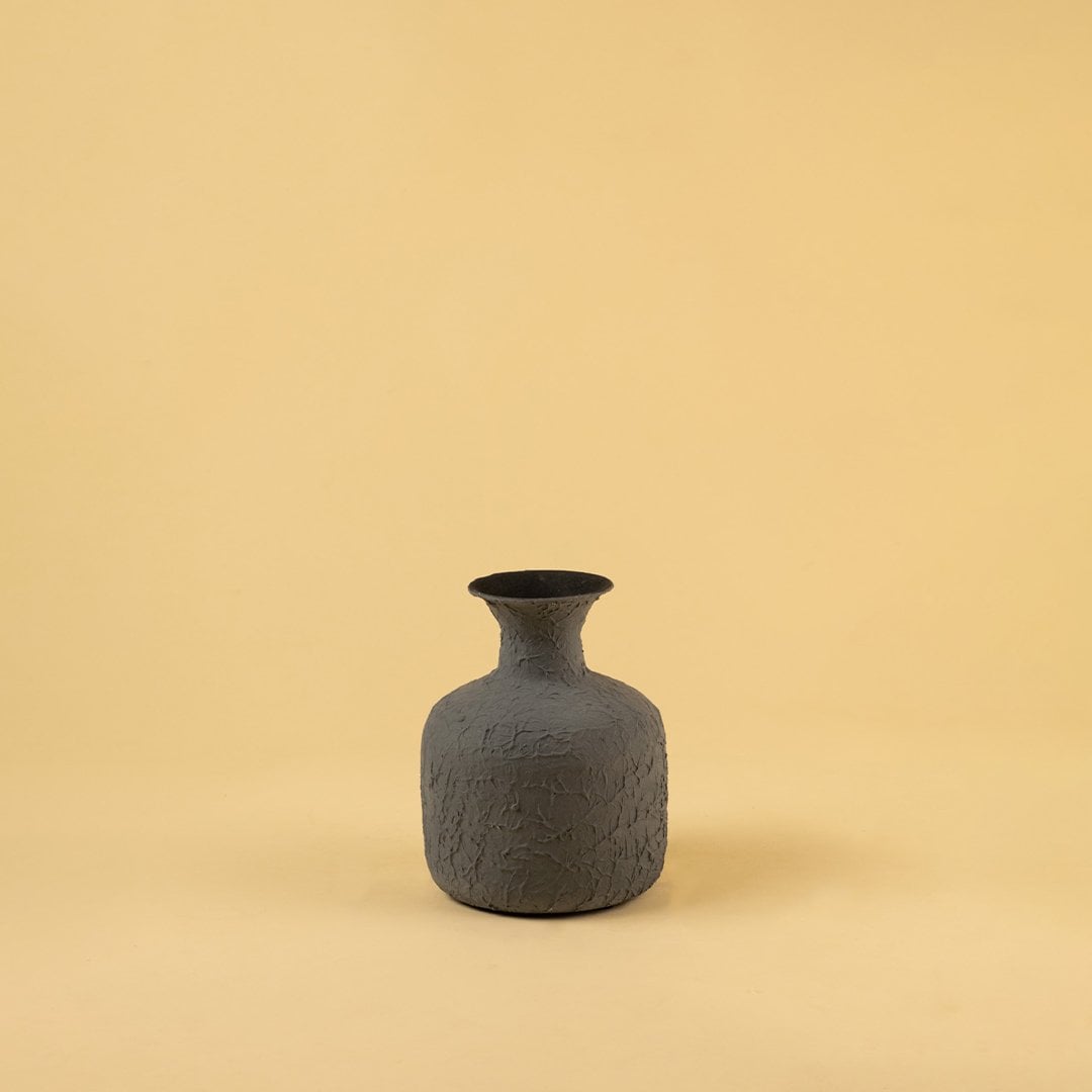 A textured grey vase standing on a light background with soft shadows highlighting its handcrafted finish and minimal organic form.