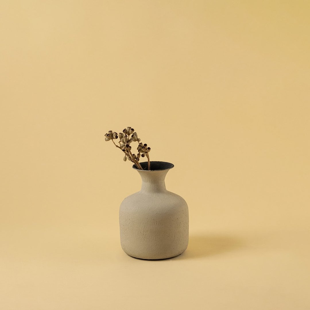 A calm interior scene shows a beige textured vase styled with dried stems bringing a warm earthy aesthetic that enhances the simplicity of the soft background.